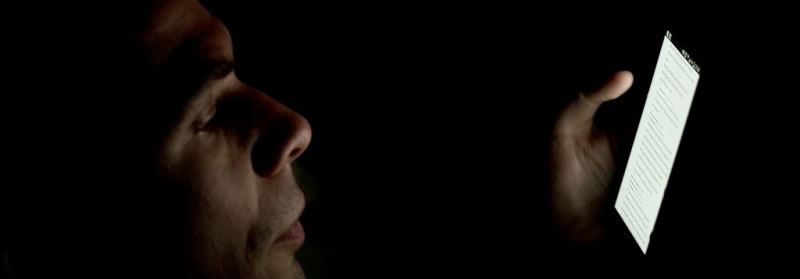 Man in darkness looking at glowing phone screen.